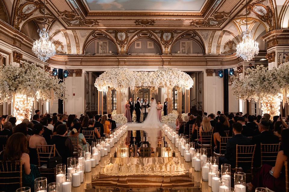 A candlelit aisle leading to a floral chuppah in a grand ballroom