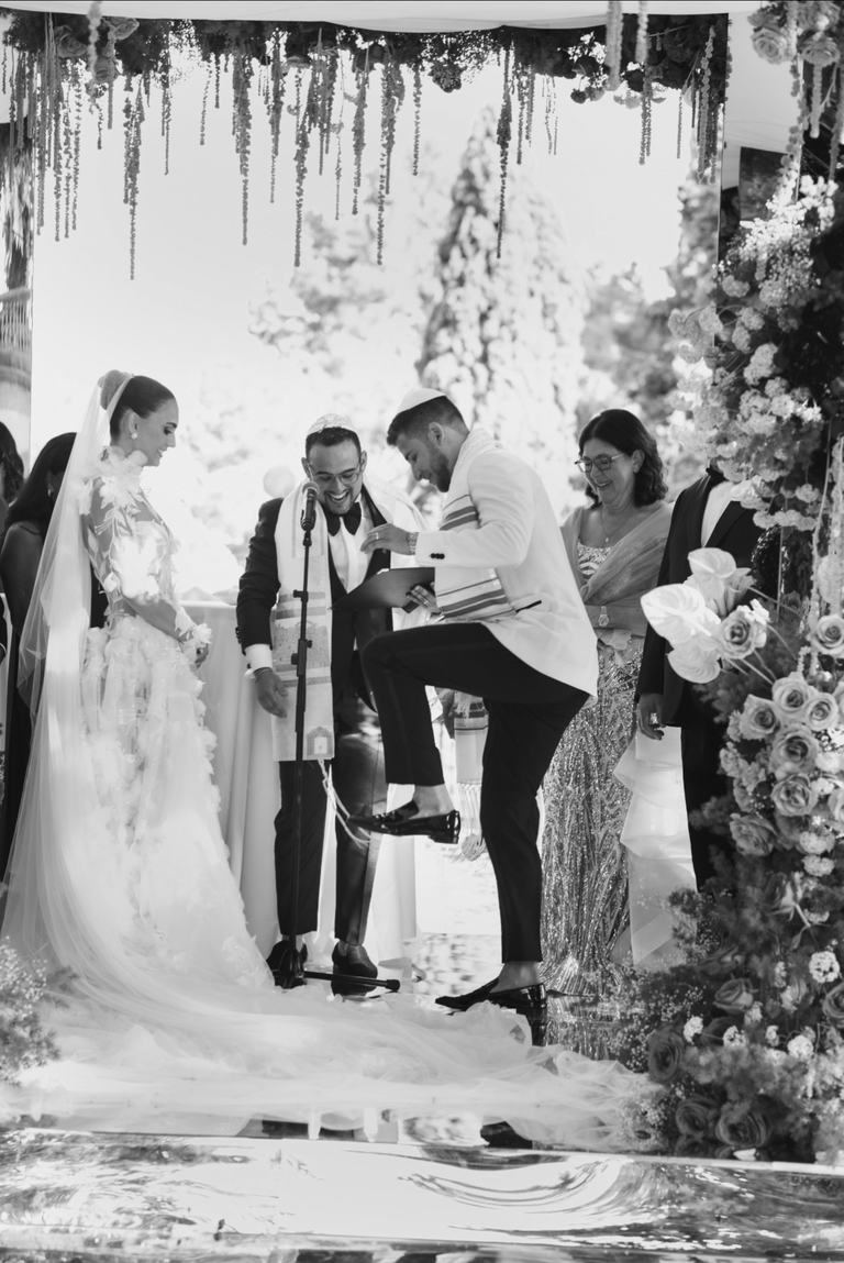 Black and white photo of a groom raising his foot to break the glass at the end of a Jewish wedding ceremony