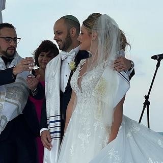 A couple shares the kiddush cup during a beachside Jewish wedding ceremony