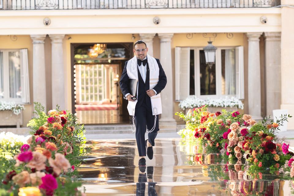 Todd Bronshtein walking down a flower-lined aisle in a tallit before a wedding ceremony